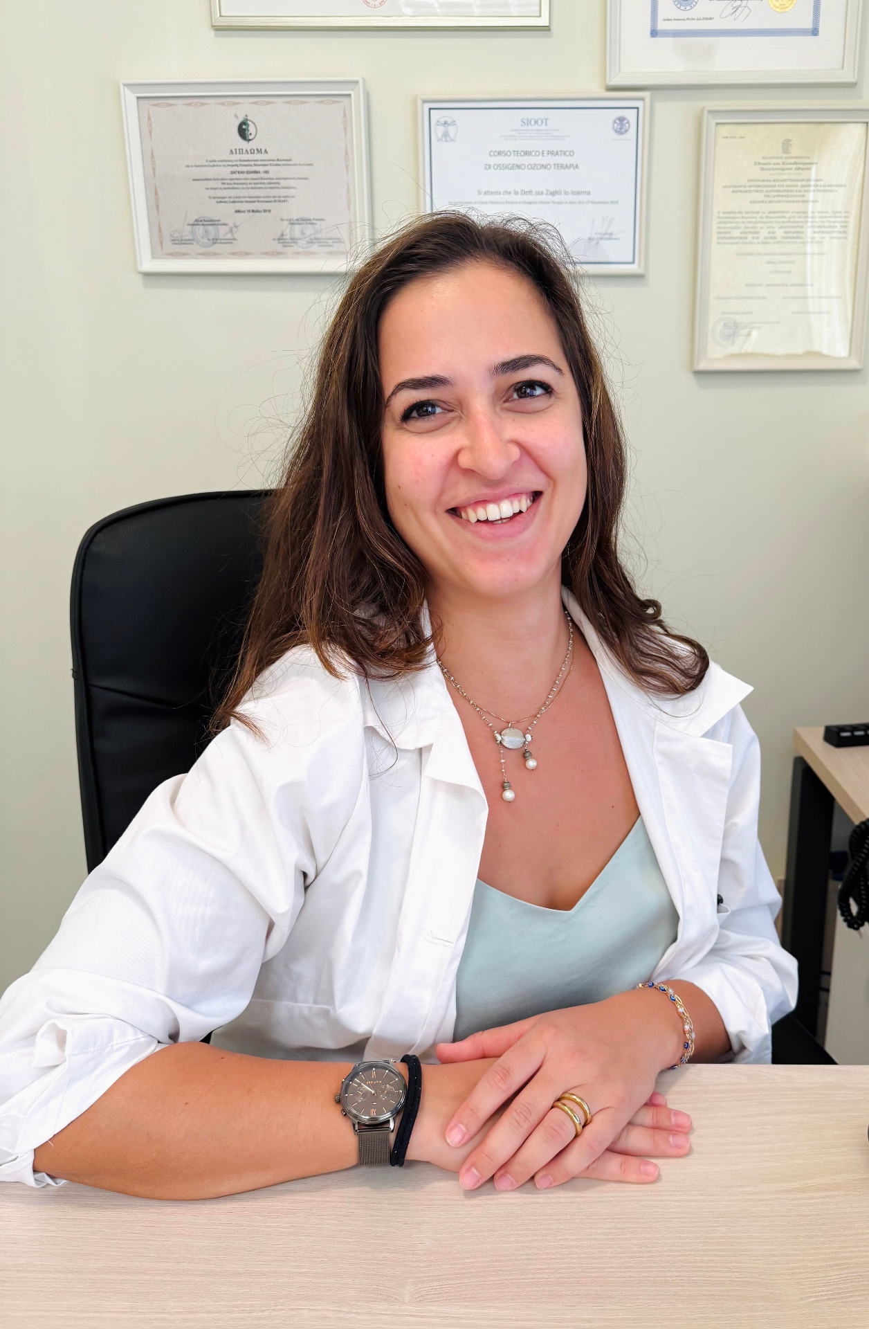 Η Δρ. Ζάγκλη Ιωάννα-Ηώ στο ιατρείο της, χαμογελαστή, φορώντας λευκή ιατρική μπλούζα
